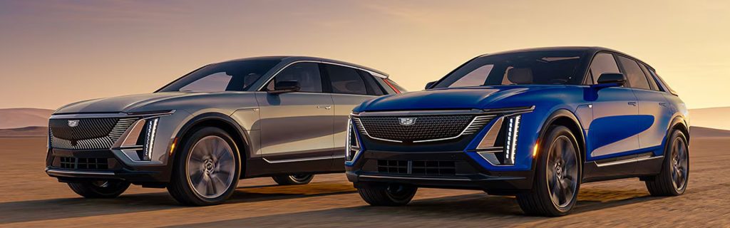 Two sleek Cadillac SUVs drive side by side at sunset.