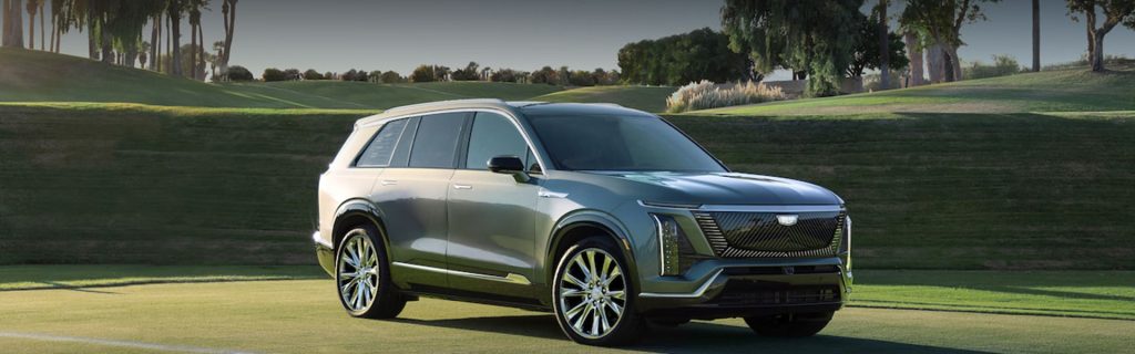 Silver Cadillac VISTIQ electric SUV parked on a manicured golf course, showcasing its sleek design and distinctive front grille.