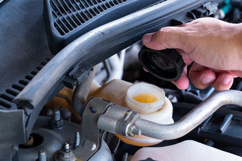 Mechanic's hand opening an oil filler cap on a car engine.